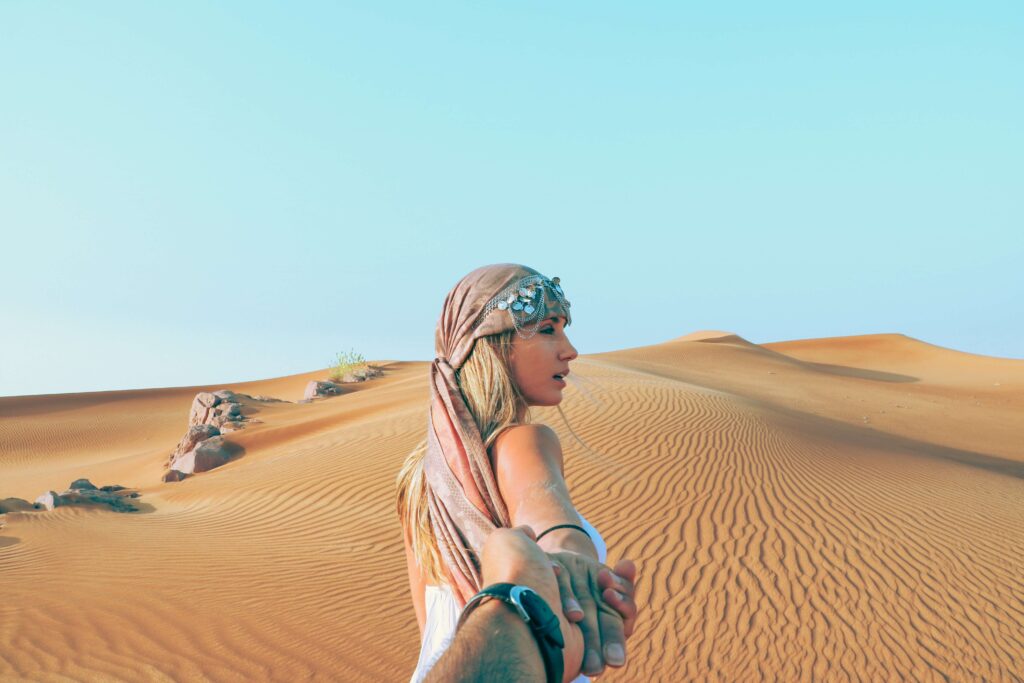Eine hübsche Frau mit Kopftuch wandert durch die Wüste der UAE und hält dabei die Hand ihres Freundes.